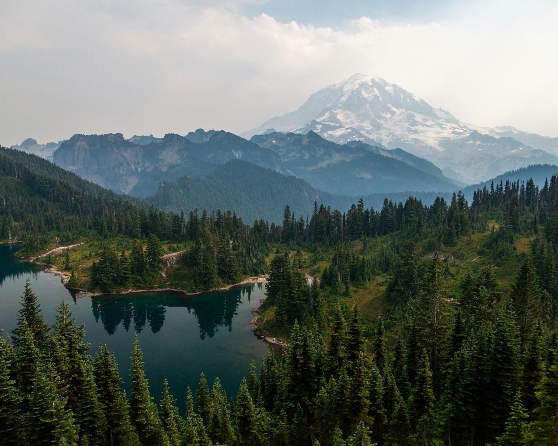 Mountain lake surrounded by evergreen forest, with a snow-capped peak in the background