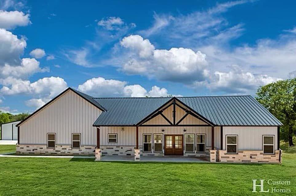 A large white house with a metal roof is sitting on top of a lush green field.