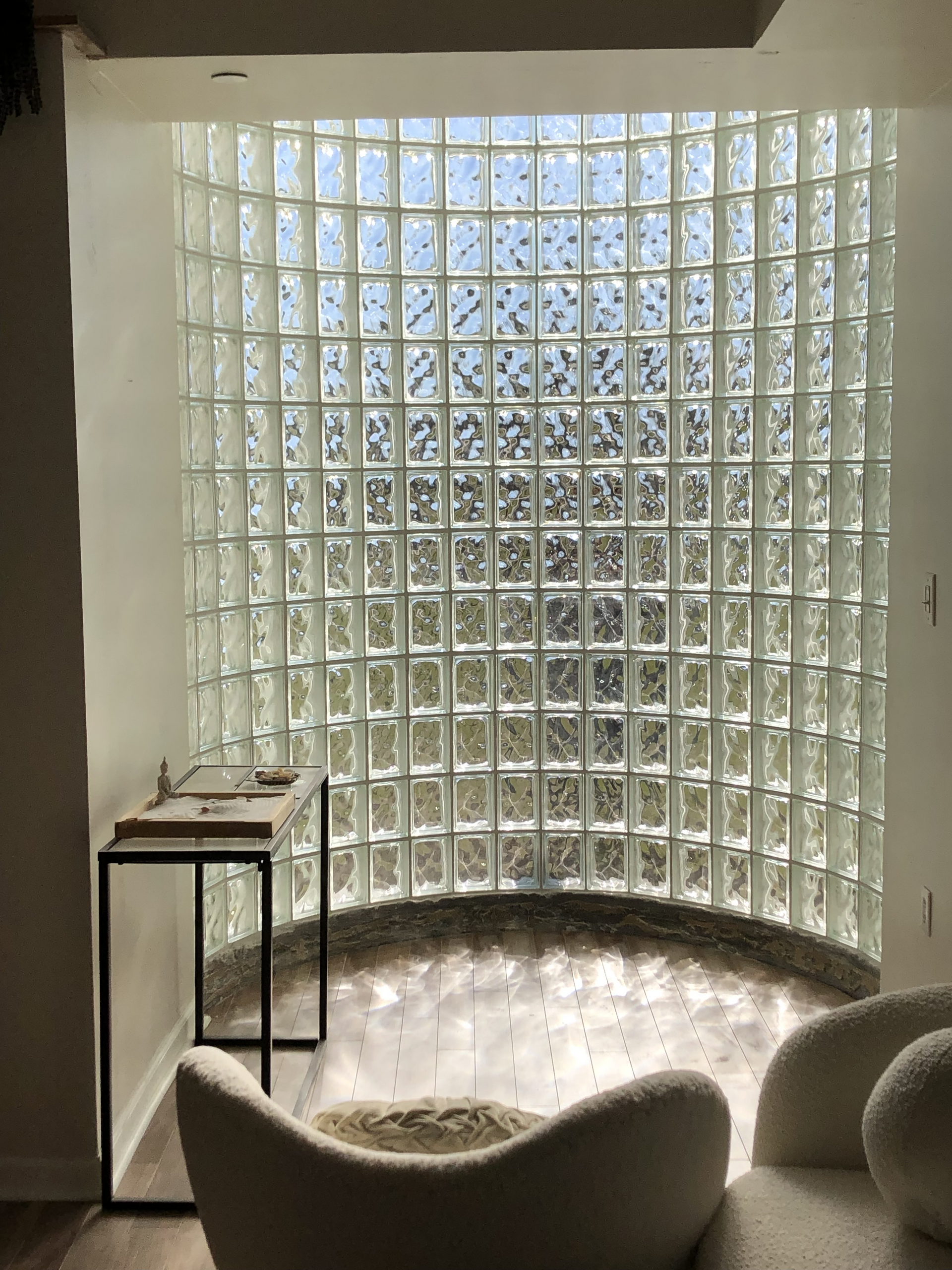 Curved glass-block wall illuminating a modern corner with a small table and sculptural chair
