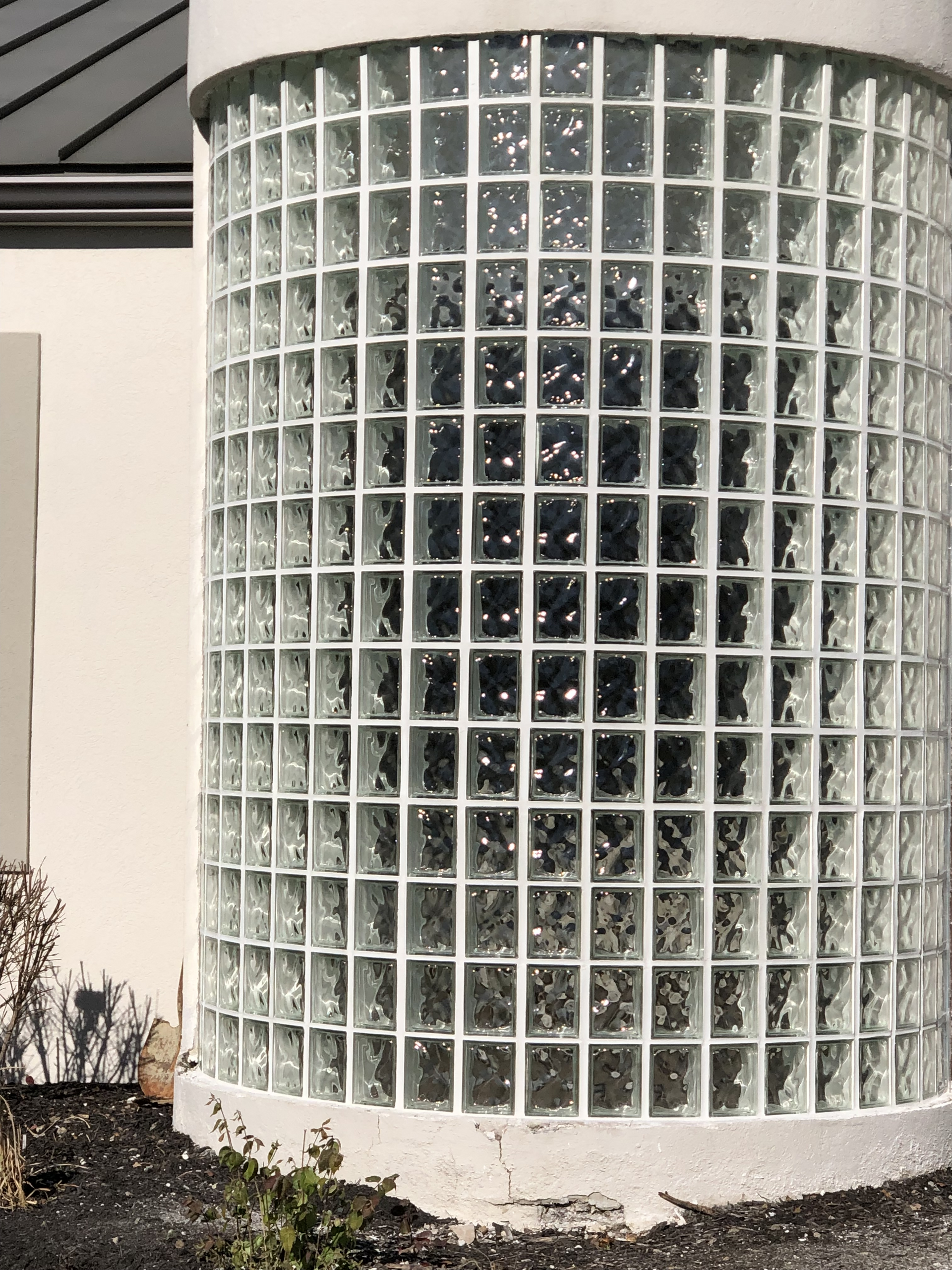Curved glass-block building wall with a grid of translucent panes and a white base outdoors