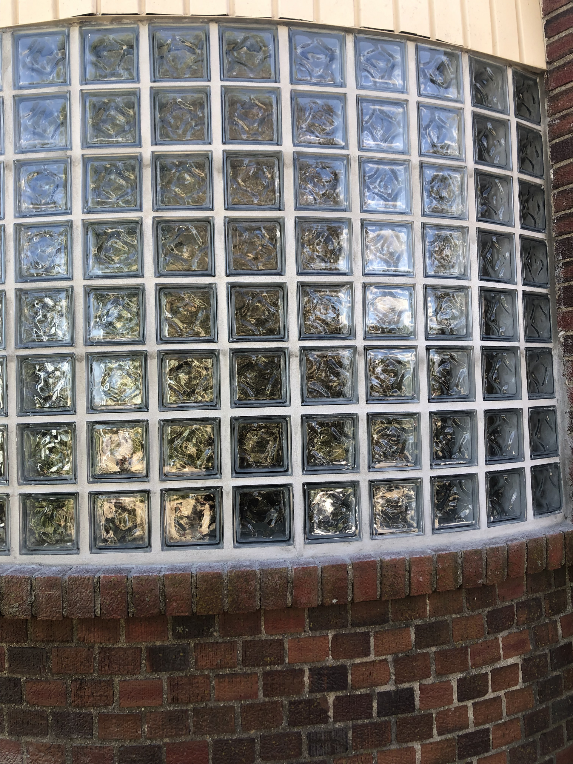 Curved glass block wall with a brick base and beige siding above
