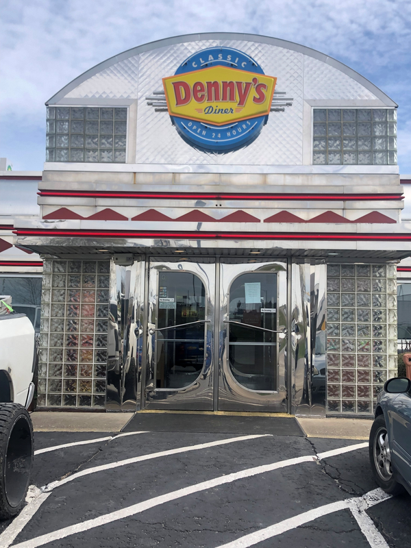Denny’s restaurant entrance with glass doors and red-and-white striped awning under the sign.