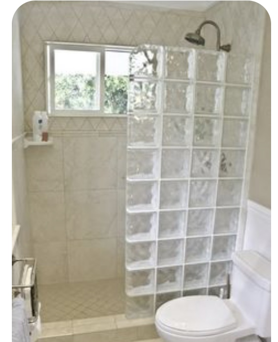 Small bathroom with tiled shower, glass block wall, window, and toilet.