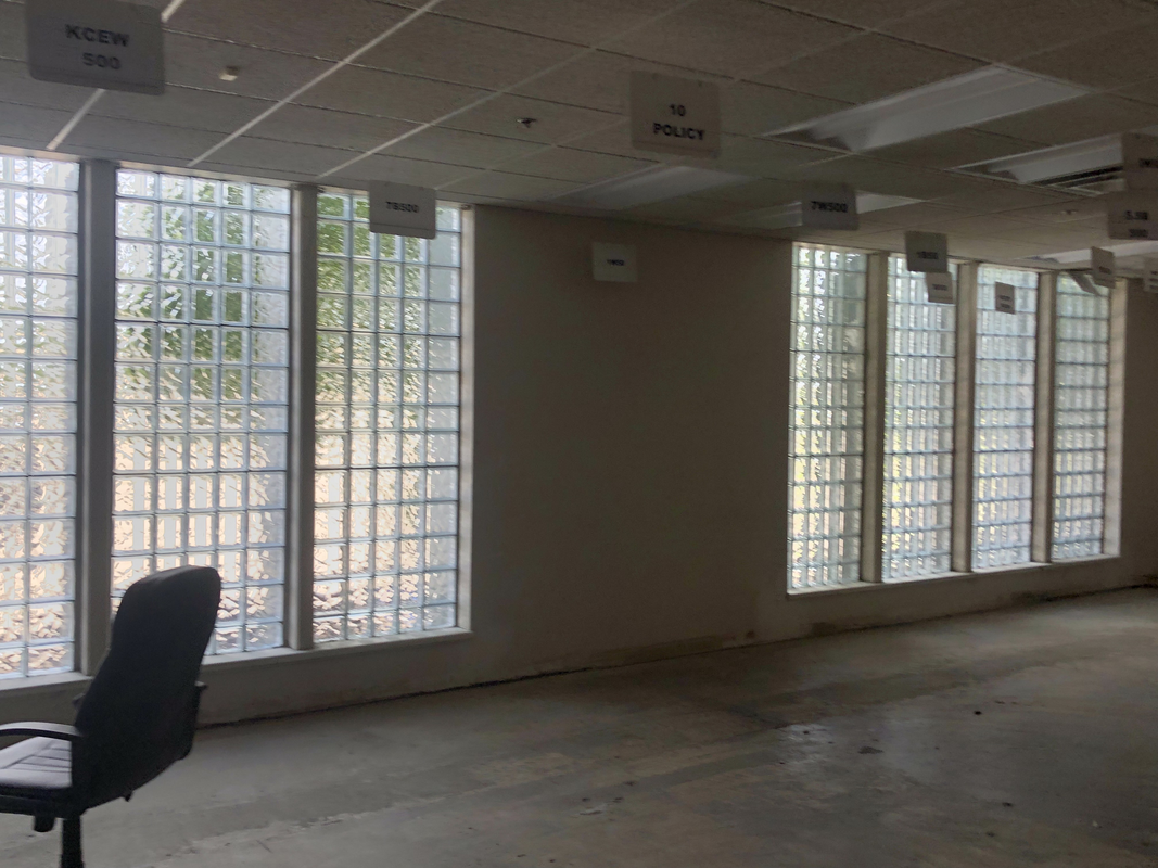 Empty room with large glass-block windows, a chair on the left, and a concrete floor