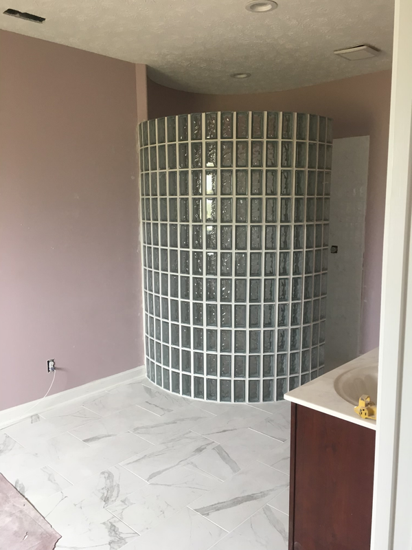 Empty room with a curved glass-block wall, pale pink walls, white floor, and a dark cabinet on the right.