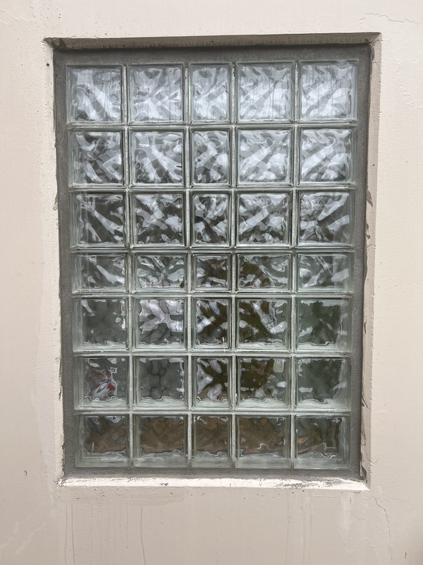 Small frosted glass block window in a beige wall, reflecting trees outside