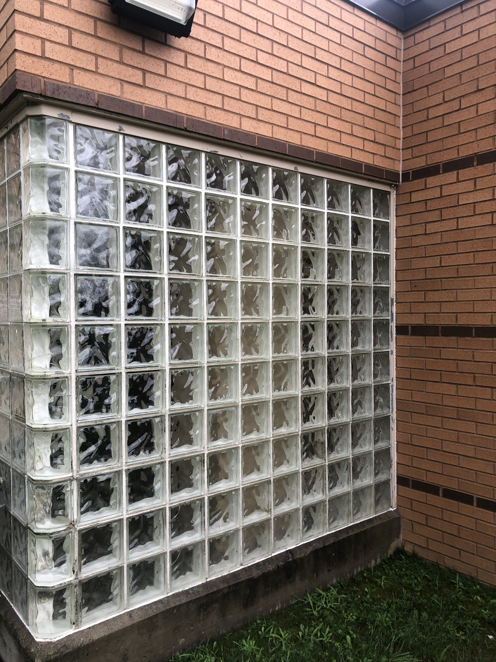 Glass block window set into a brick wall beside a small patch of grass.