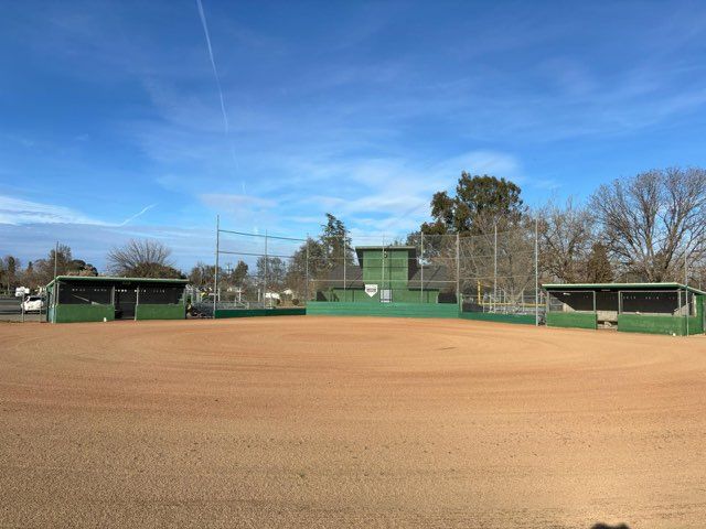 Empty baseball field with green dugouts, backstop, and a blue sky.