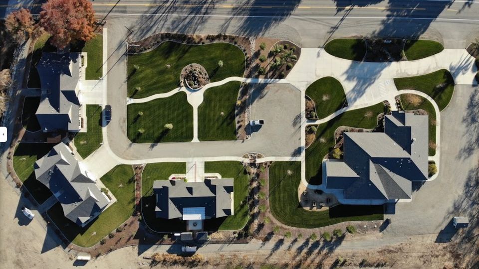 Aerial view of buildings, walkways, and landscaping. Dark roofs, green grass, and gray concrete.