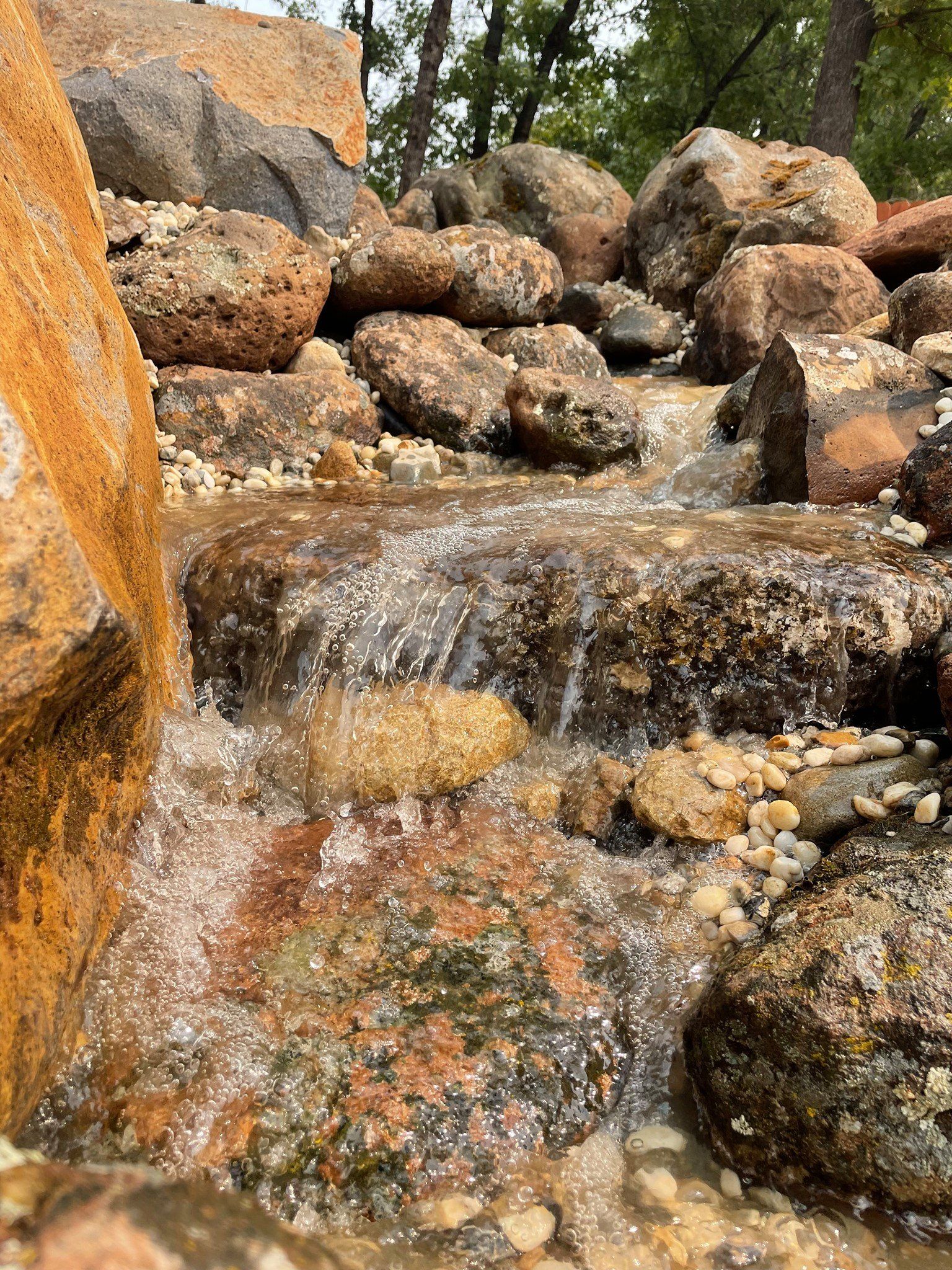 Water cascading over rocks in a small stream; brown and gray hues with small pebbles.