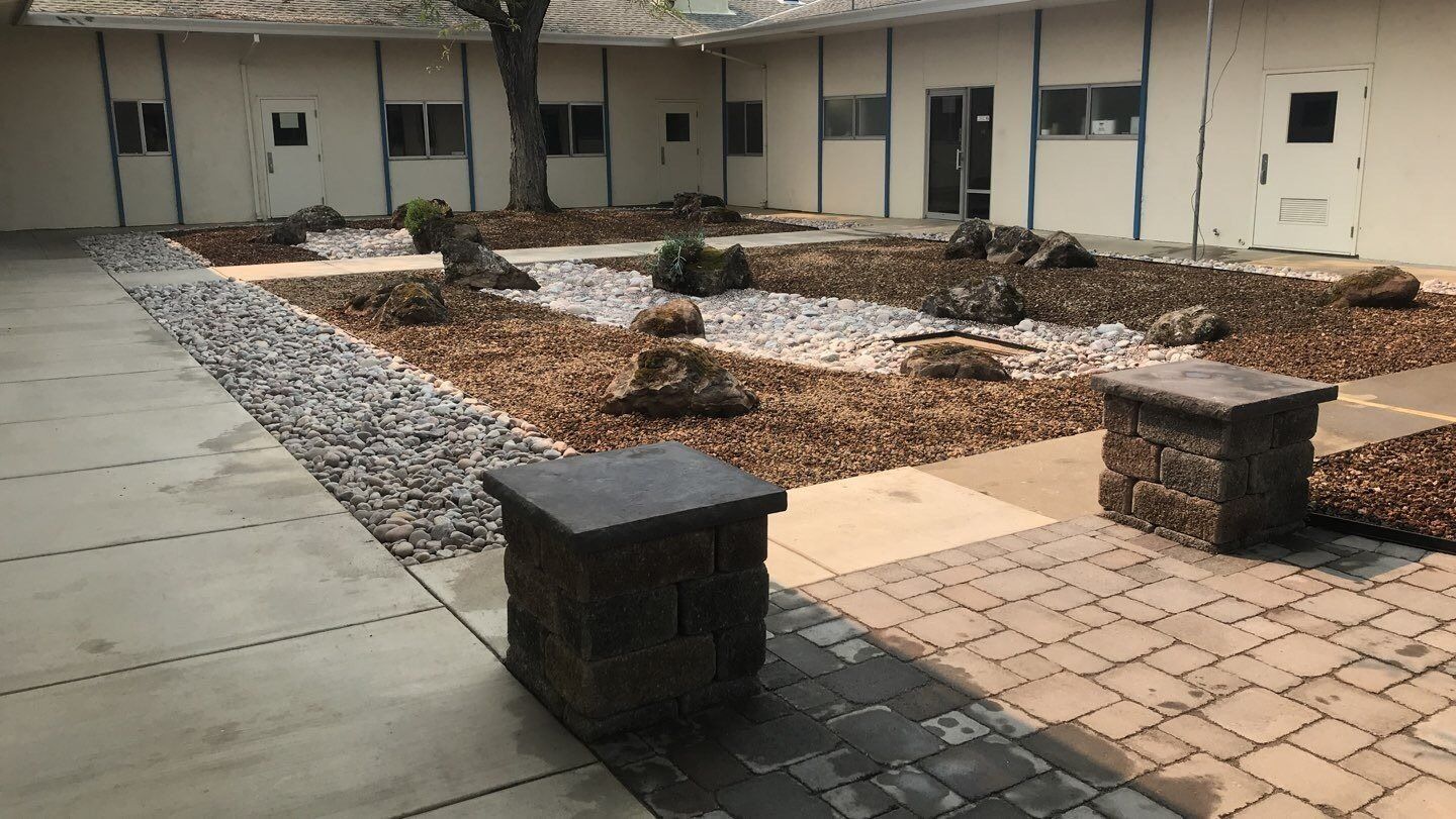Courtyard with rock garden, pathways, concrete pillars, and light-colored buildings.