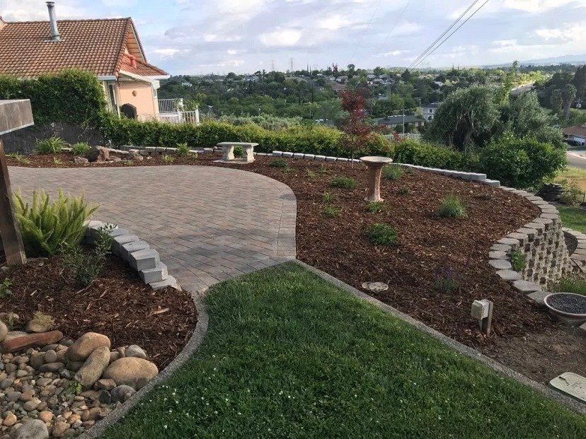 Curved driveway and lawn in a landscaped yard; house in the background, view of a distant cityscape.