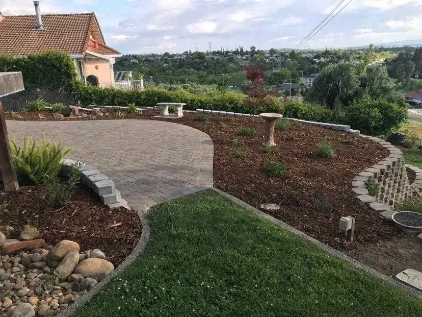 Curved driveway and garden with bench, birdbath, and retaining wall, overlooking a distant vista.