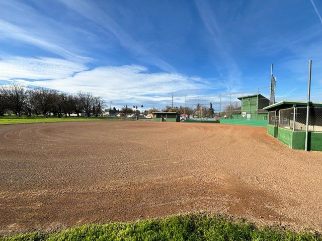 Empty baseball field on a sunny day with green dugouts and blue sky.
