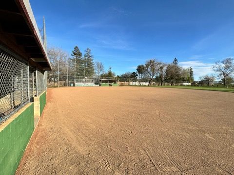 Empty baseball field with brown dirt, green dugout, and blue sky.