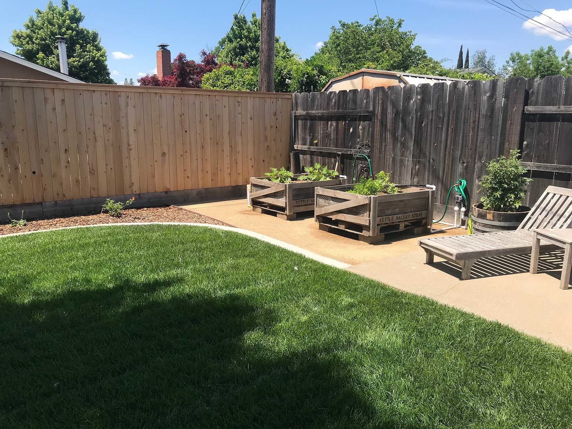 Backyard with lawn, wooden fences, concrete patio, raised garden beds.