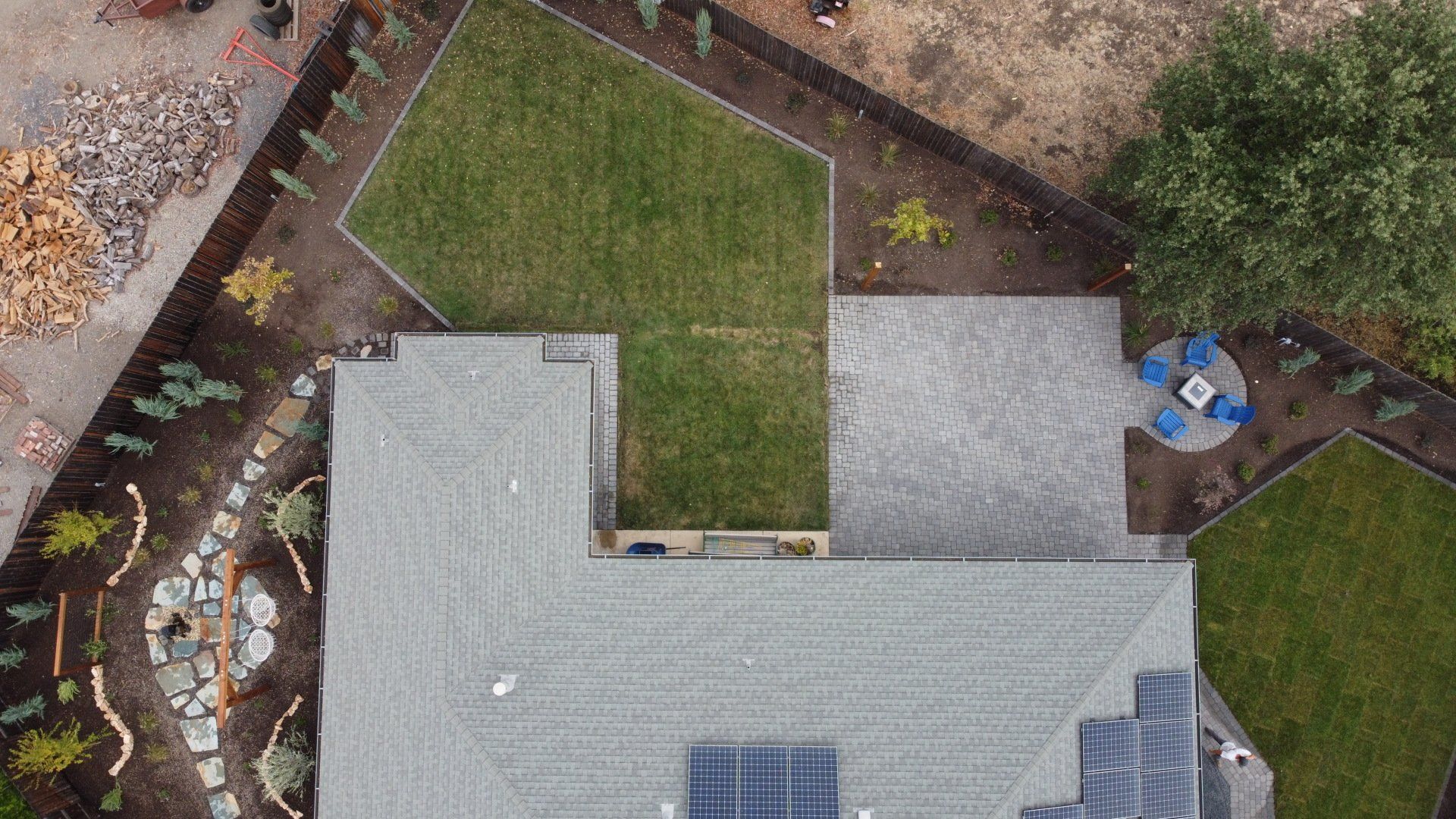 Overhead view of a house with a gray roof and landscaping, including patios, lawns, and trees.
