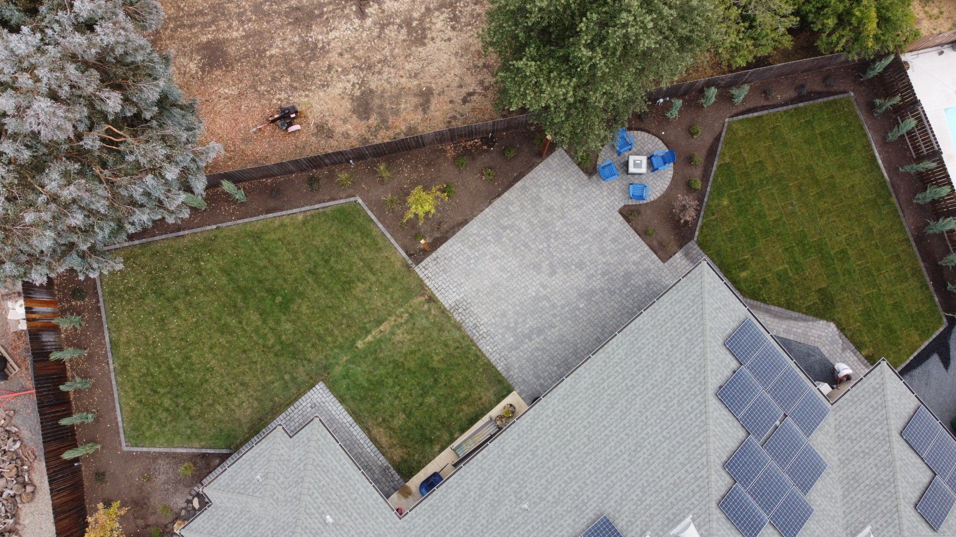 Overhead view of a backyard with a house, solar panels, patio, grass, and trees.