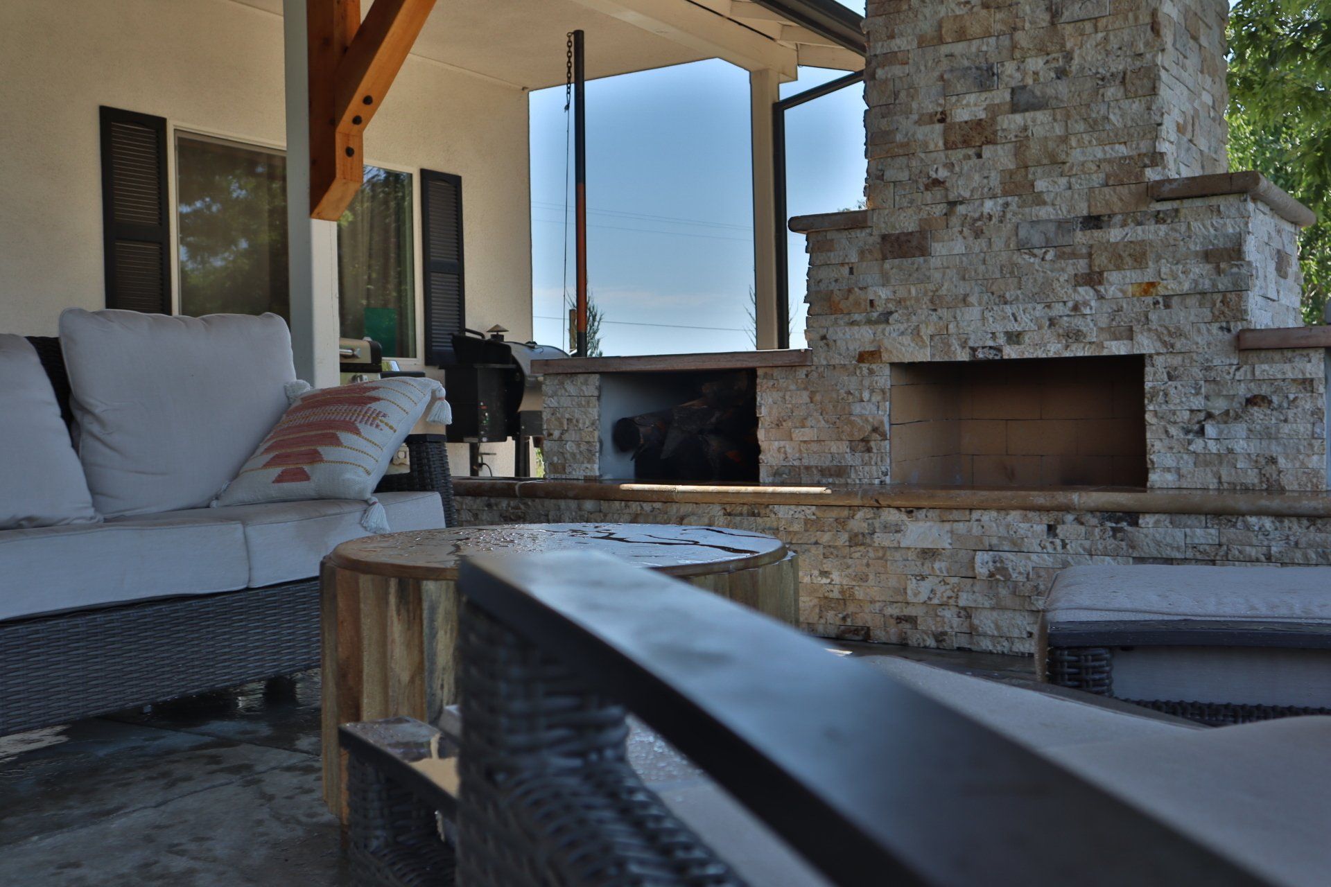 Outdoor seating area with a stone fireplace, sofa, and small wooden tables.