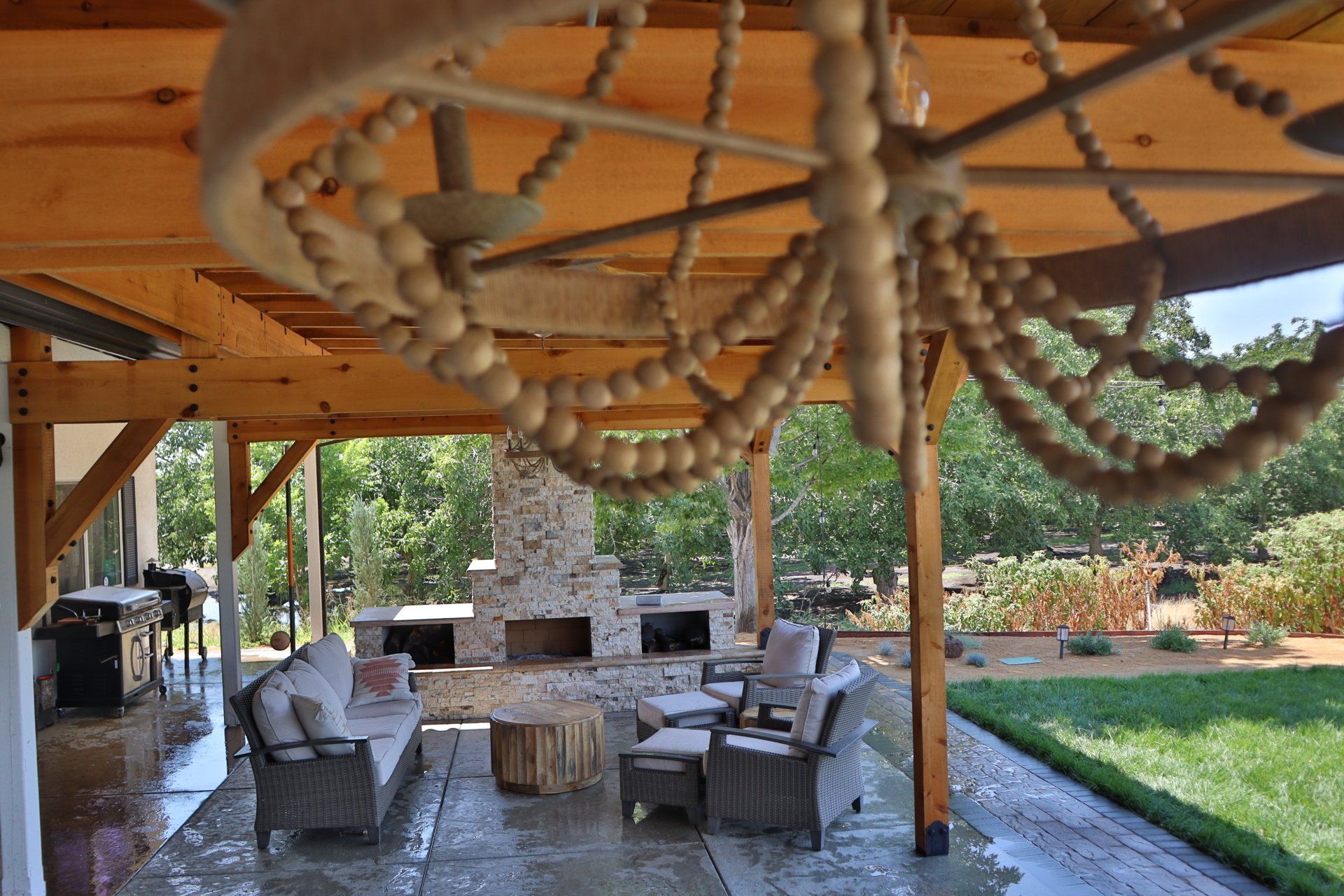 Beaded chandelier over an outdoor seating area with fireplace, wood beams, and green lawn.