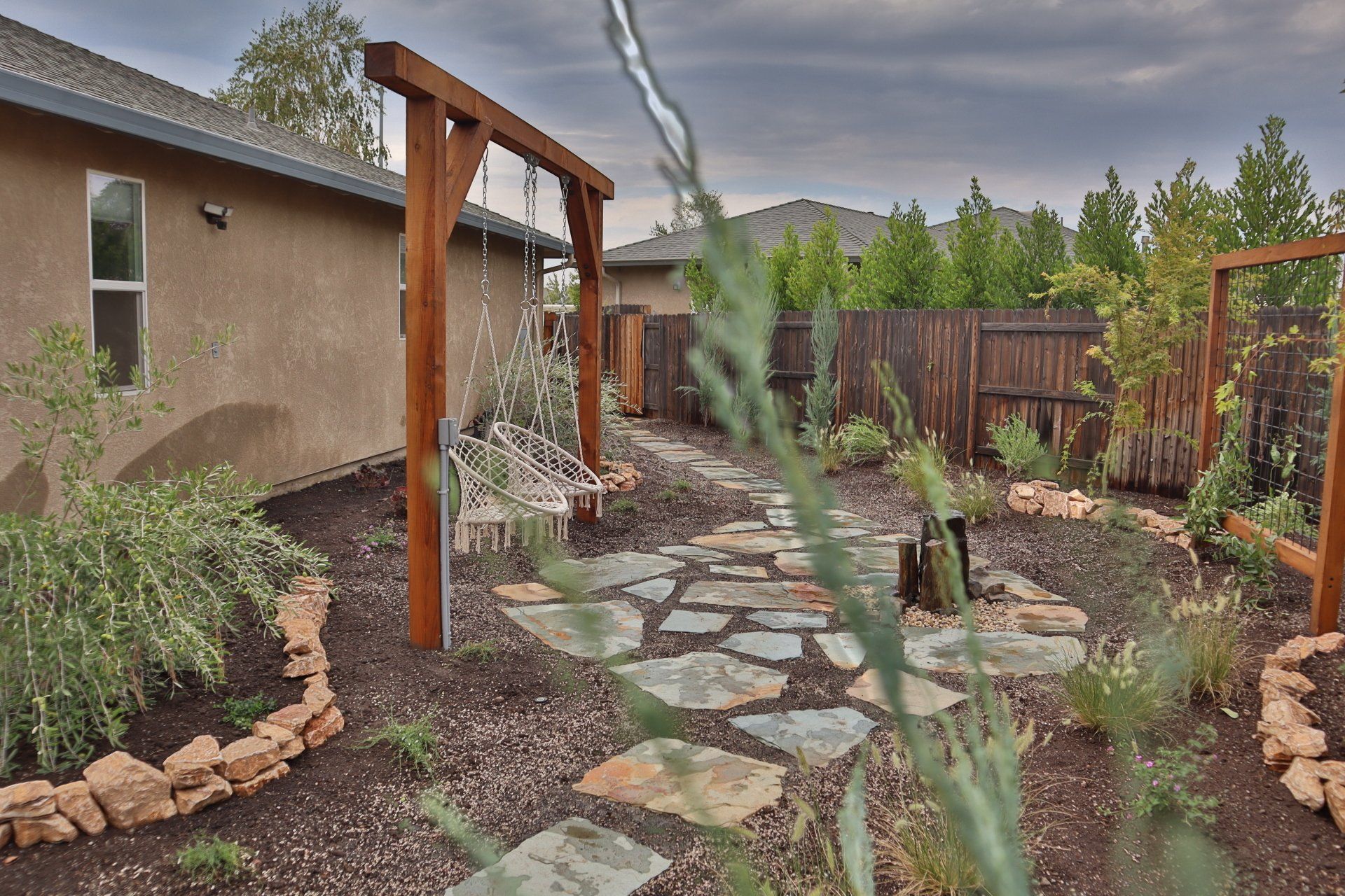 Backyard with wooden swing, stone path, landscaping, and wooden fence.