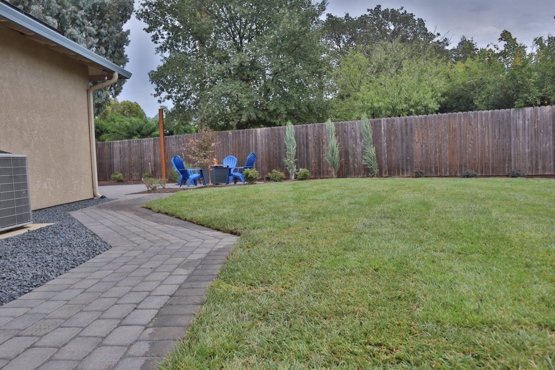 Backyard with a brick path, green lawn, wooden fence, and blue patio furniture.