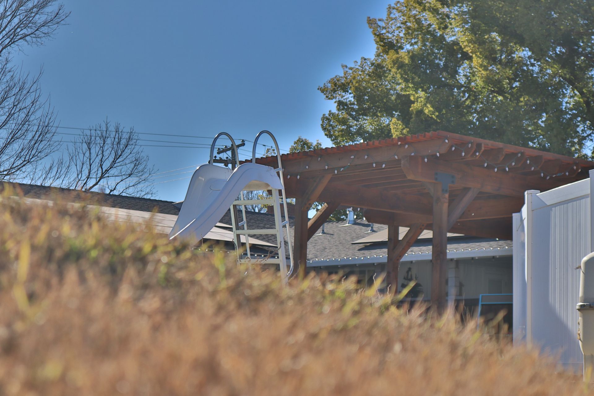 Swimming pool slide next to a wooden pergola with string lights.