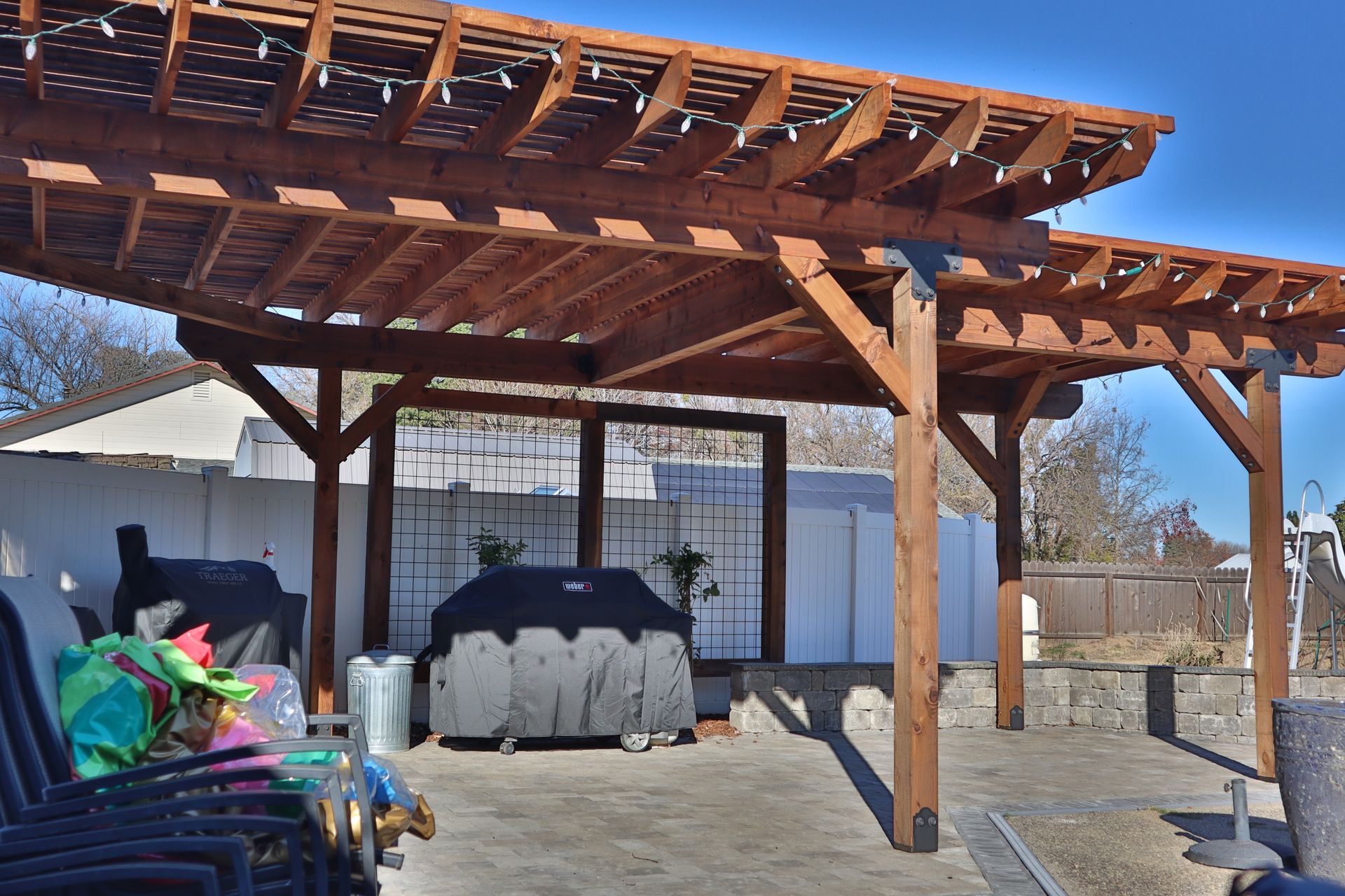 Wooden pergola over a patio with a grill and outdoor seating.