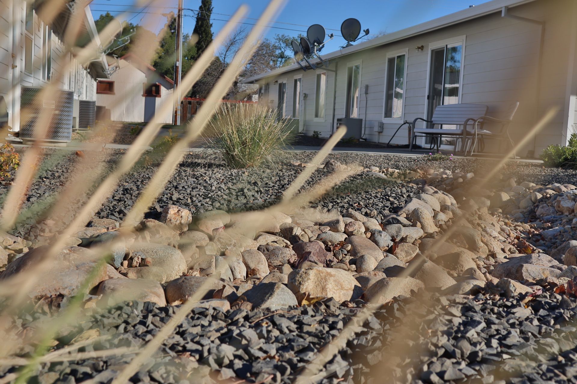 A house exterior with satellite dishes, a rock garden, and grass in the foreground.