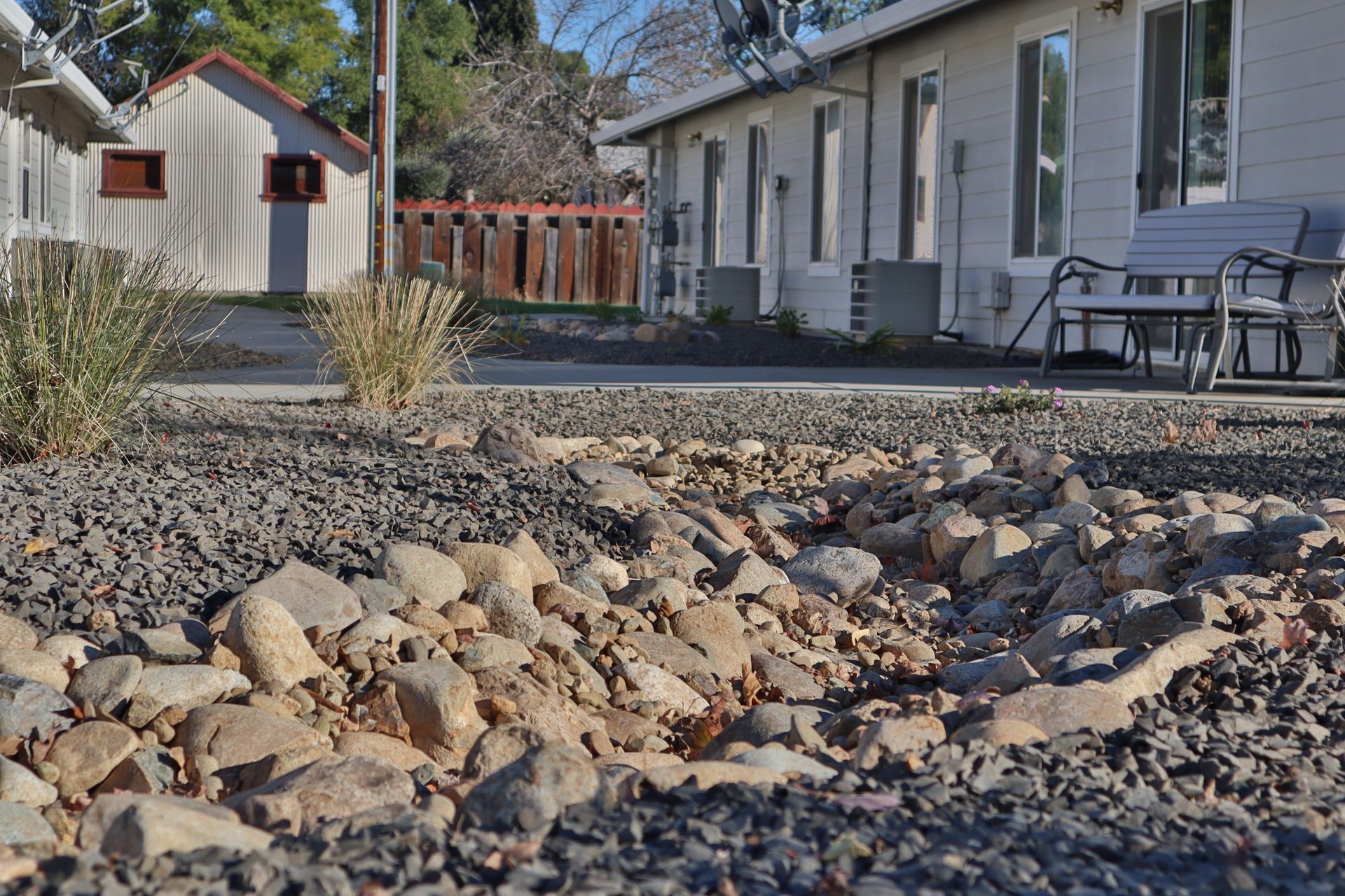 Gravel and rocks in a dry creek bed in front of a building and small shed.