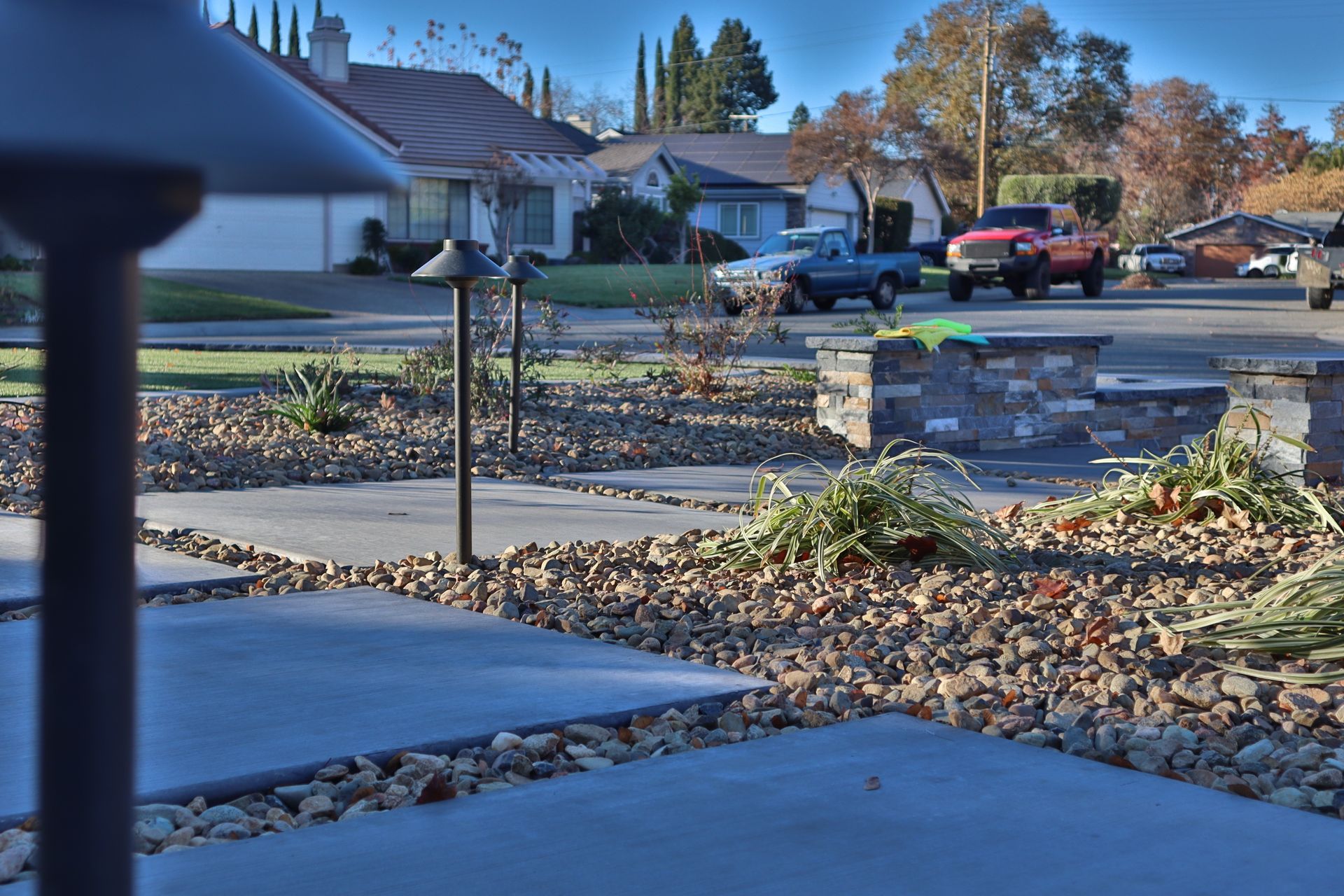 Suburban street scene with homes, landscaping, and parked trucks on a sunny day.