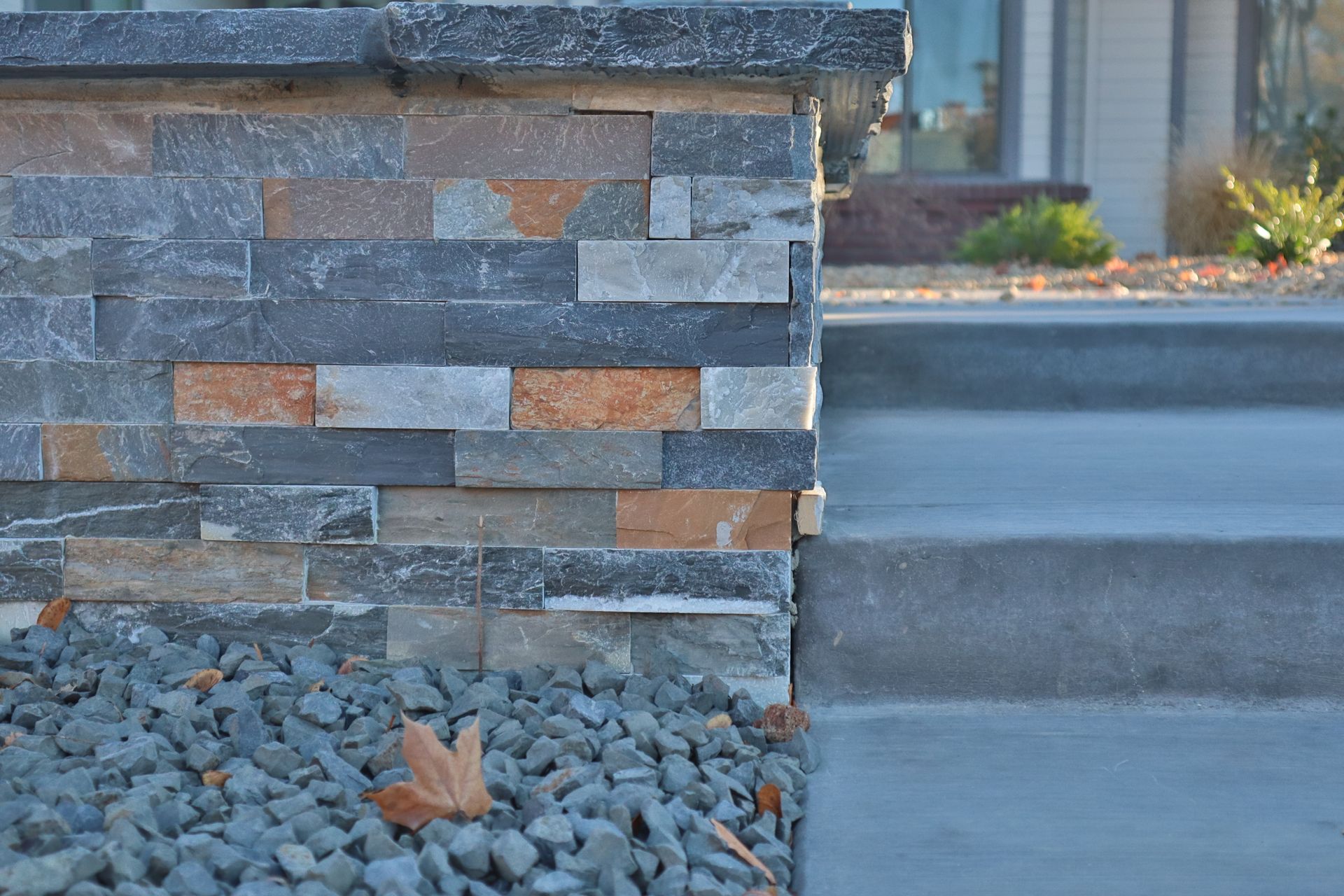 Stone facade pillar with steps and gravel, next to a concrete path; outdoors.