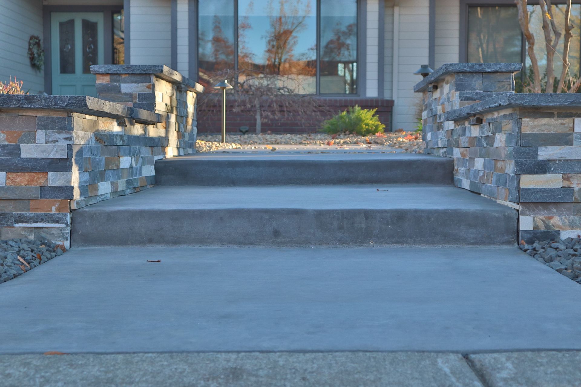 Concrete steps leading to a house with decorative stone accents on the pillars.