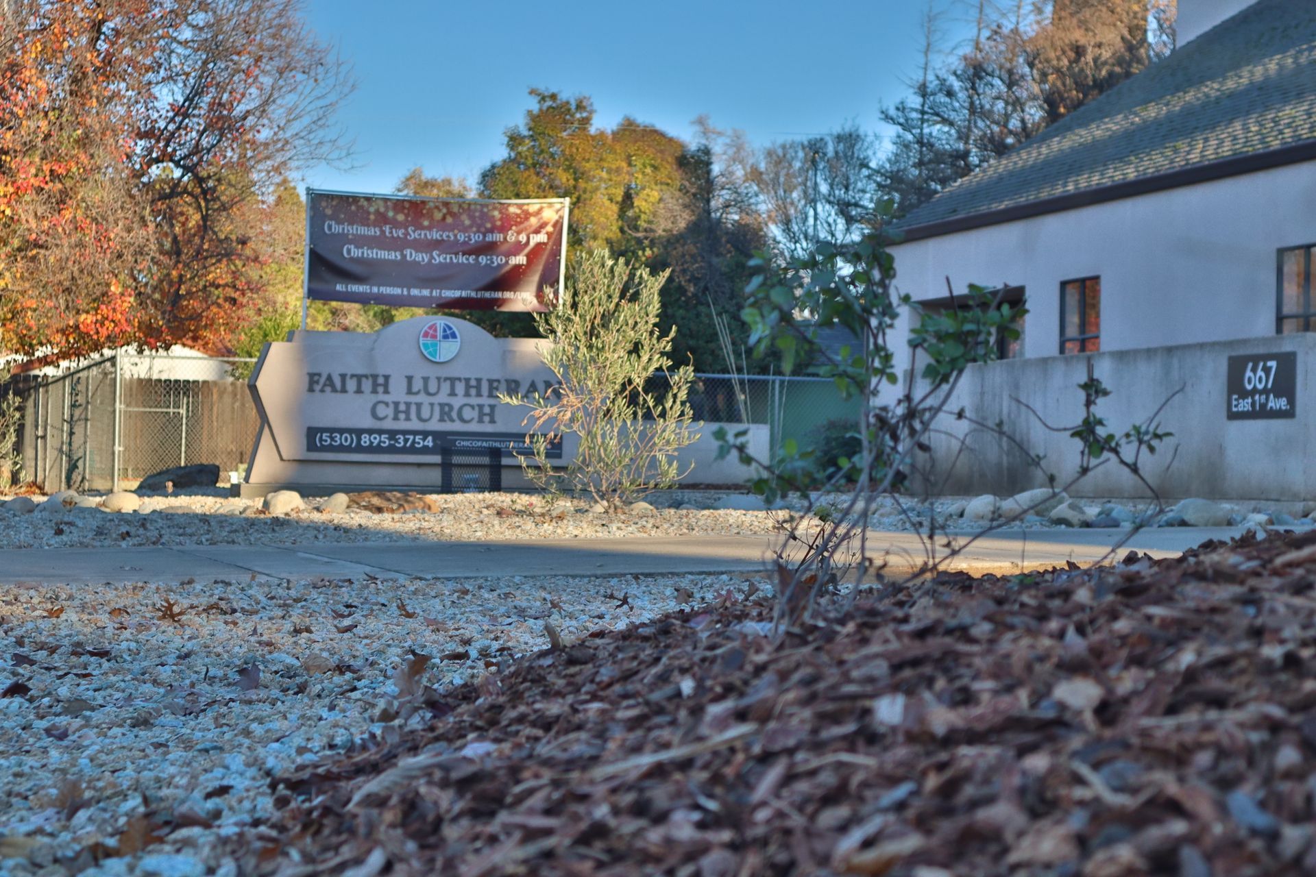 Faith Lutheran Church sign, beige building, banner, trees, and gravel road.