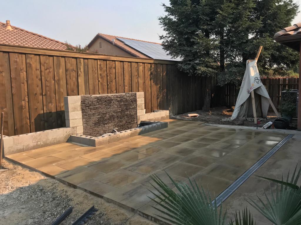 Backyard patio with water feature, wooden fence, and teepee; construction in progress.