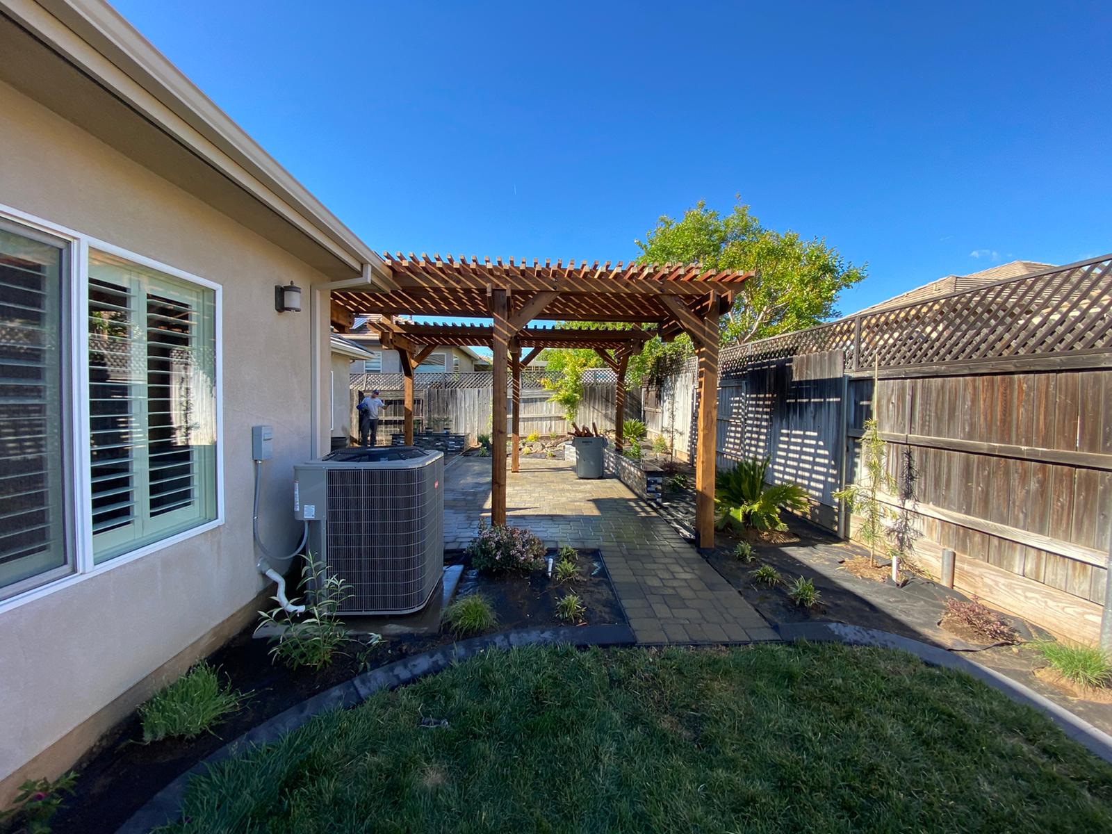 Backyard patio with wooden pergola, pathway, and landscaping.
