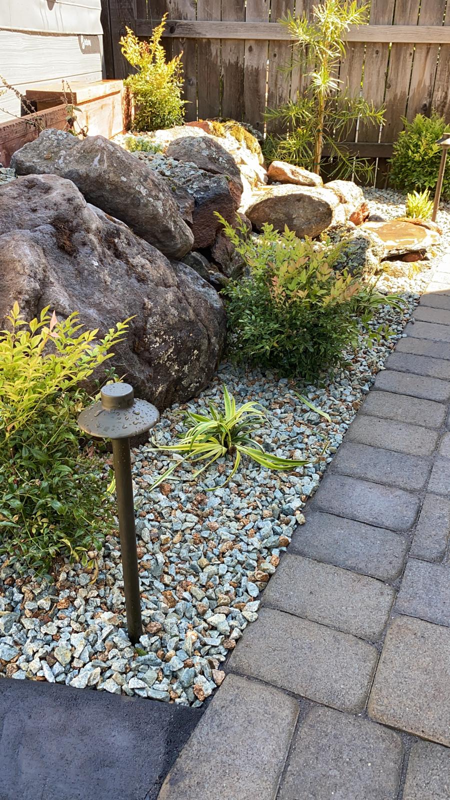 Landscaped yard with large rocks, gravel bed, paving stones, and small plants.