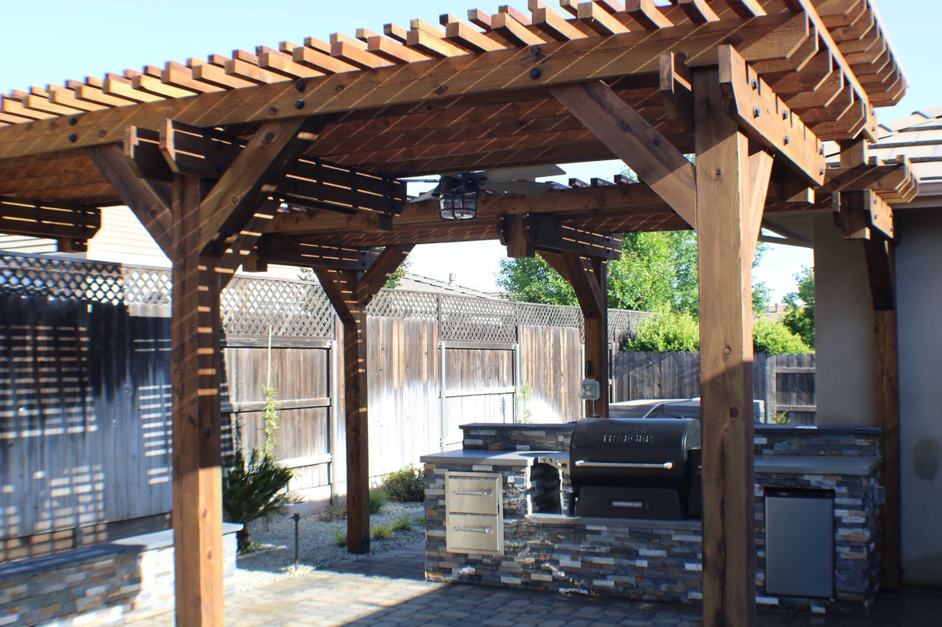 Wooden pergola over outdoor kitchen with grill and built-in features, backyard setting.