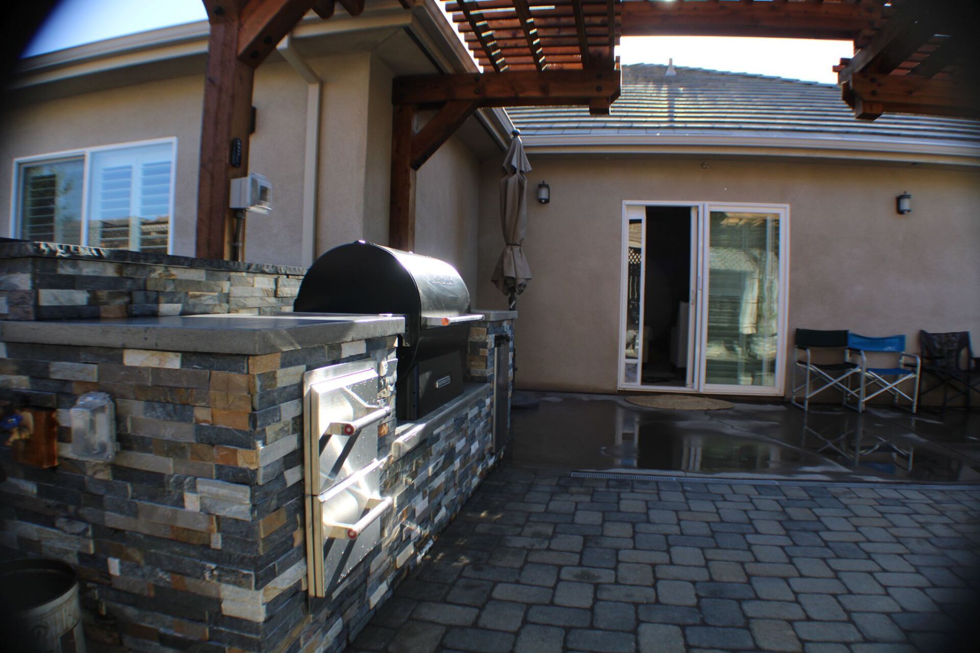 Outdoor kitchen with brick patio, built-in grill, and wood pergola.