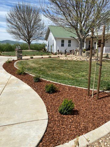 A white house with a green roof, a curved driveway, and brown mulch landscaping.