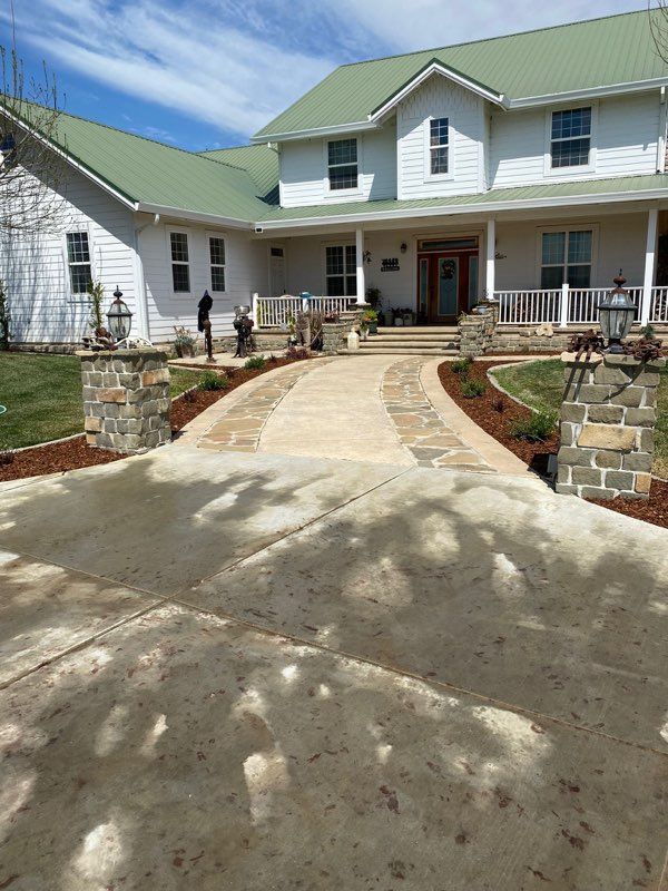 White house with green roof, a stone walkway, and a driveway leading to it.