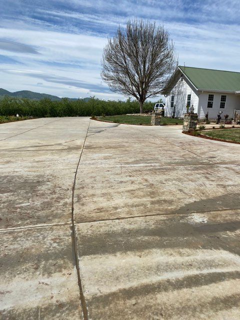 Concrete driveway leading to a white house with a green roof, tree and mountains in the background.