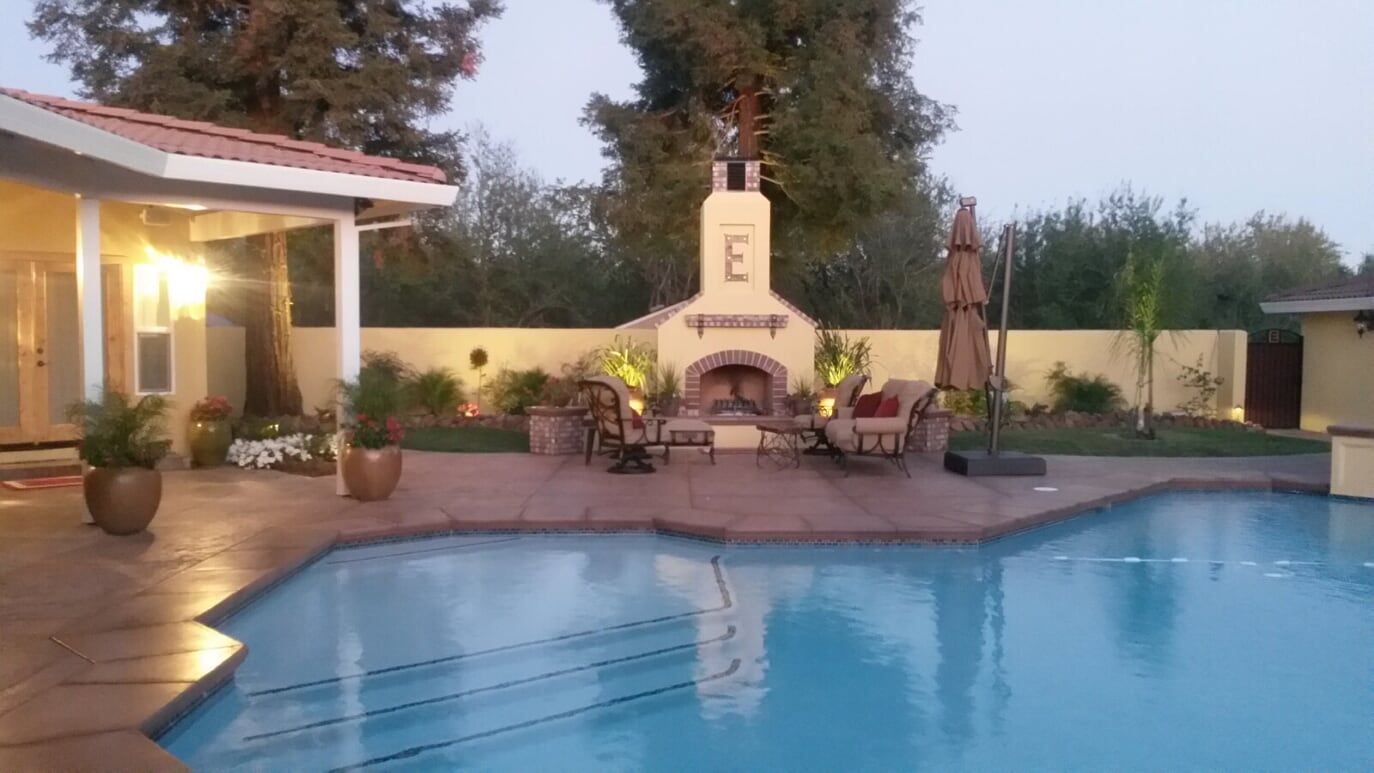 Backyard pool with a fireplace, patio furniture, and evening lighting.