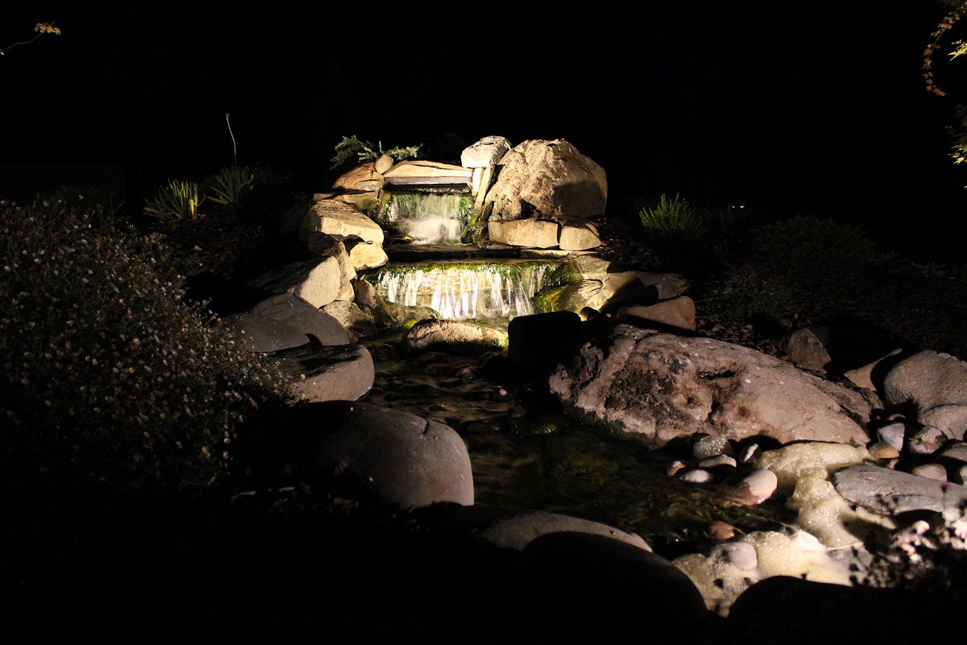Night-lit waterfall cascading over layered rocks, reflecting soft light into the water.