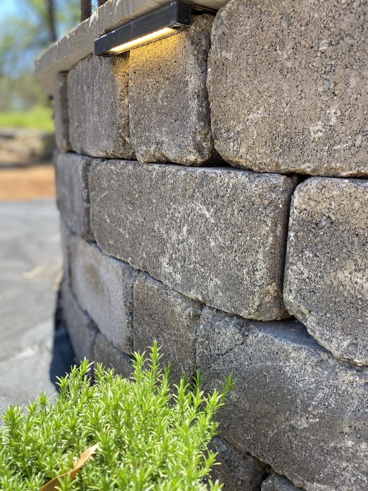 Stone retaining wall with built-in light, curved shape. Green plants in foreground.