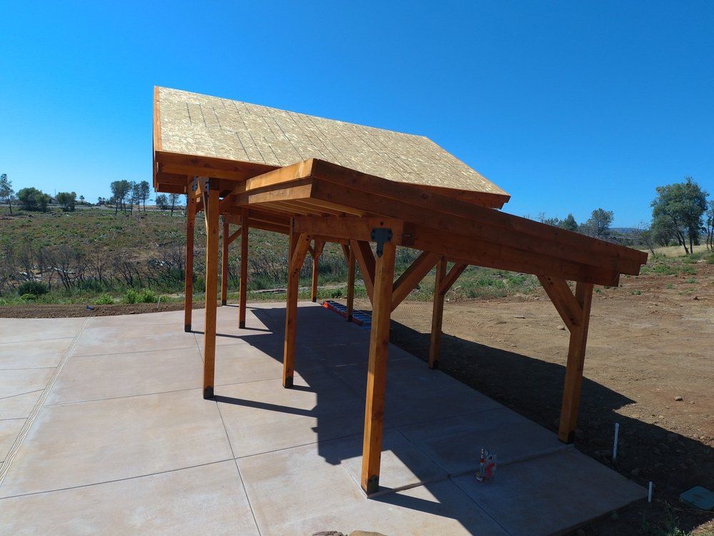 Wooden carport with straw roof on concrete, outdoors under a blue sky.