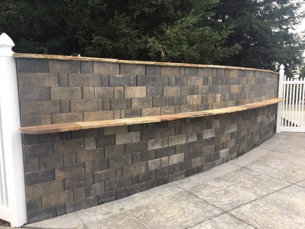 Stone block wall with wooden bar top, attached to white fence. Outdoor setting.