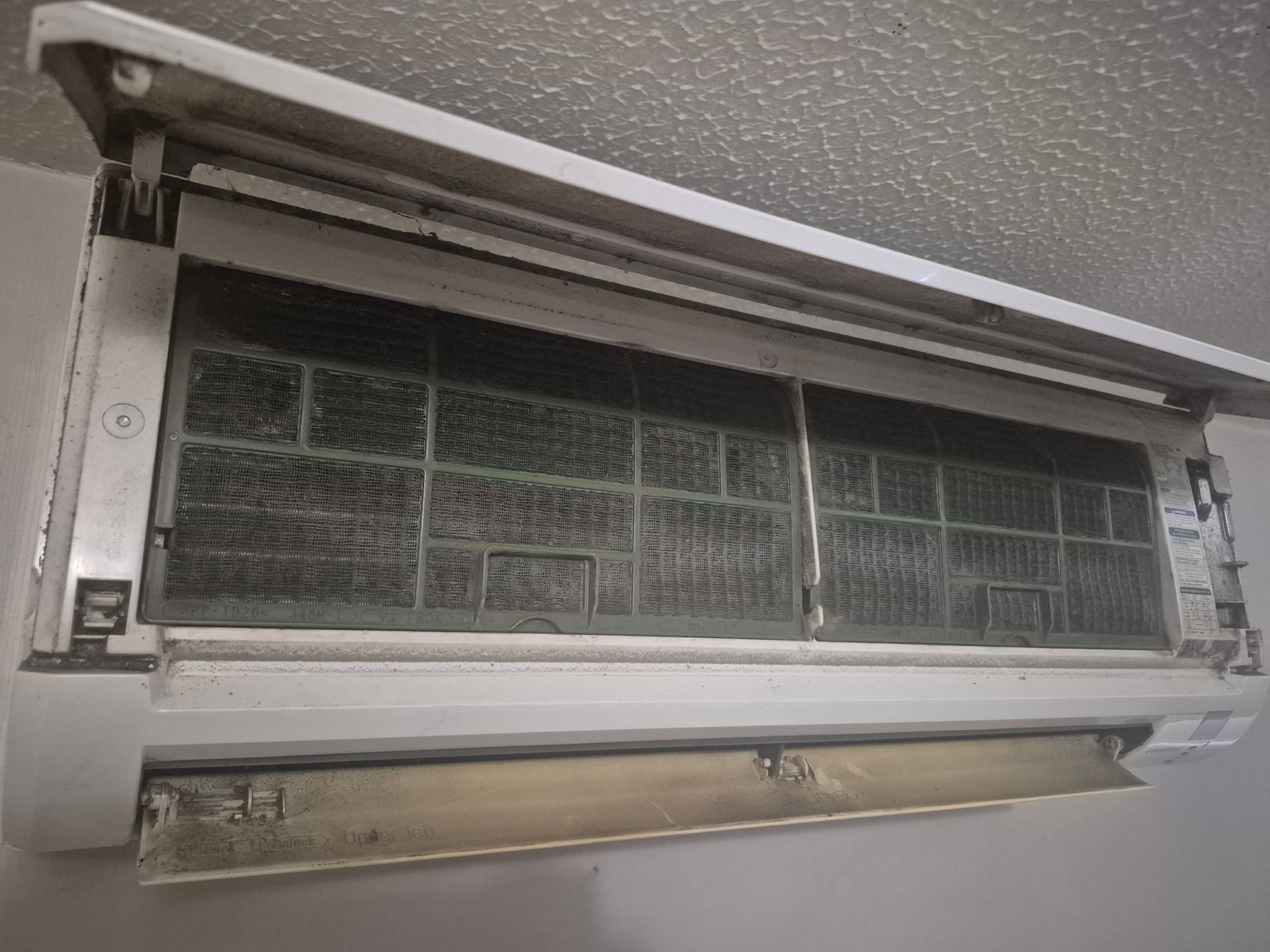 Dirty air conditioner with visible filters, mounted on a wall.