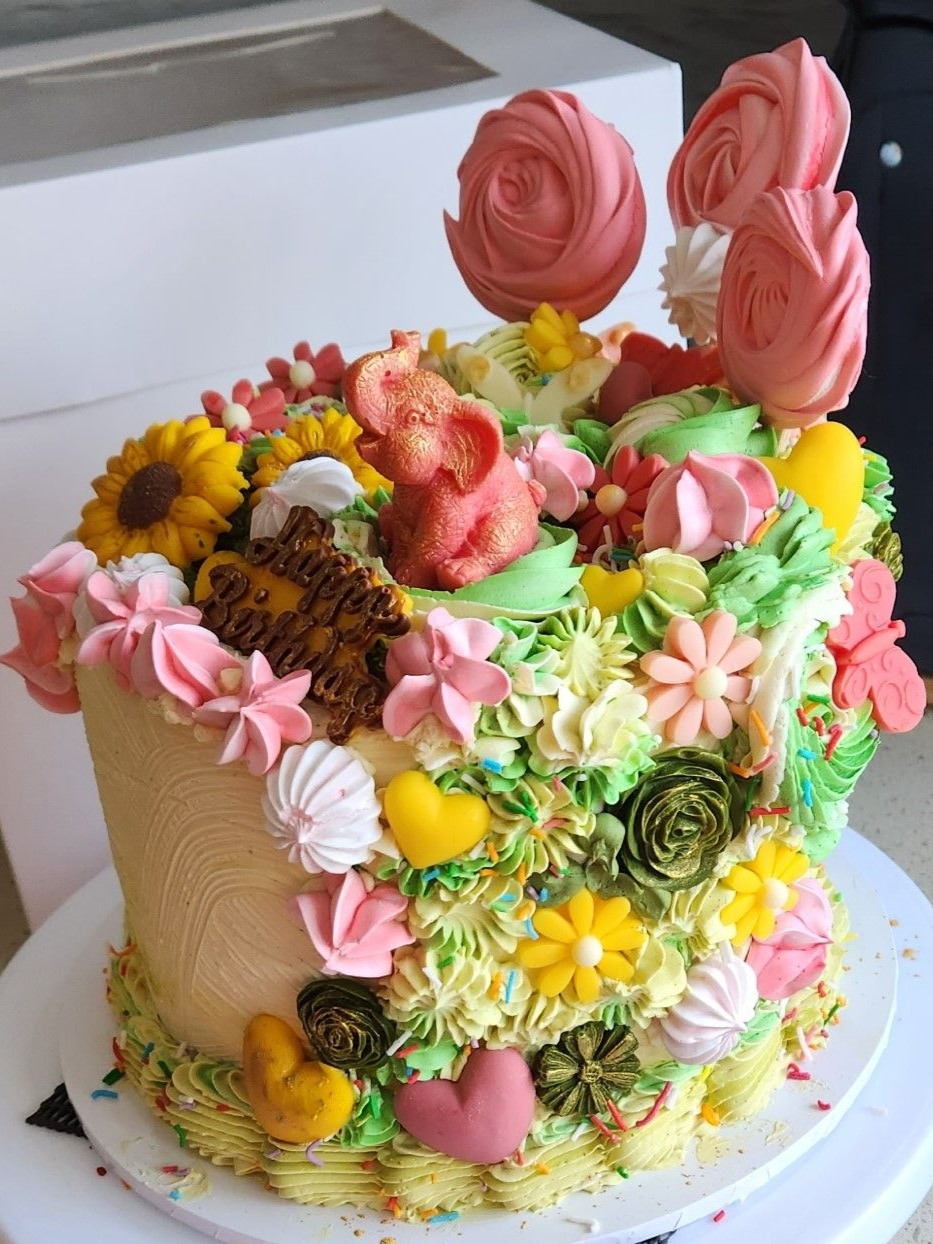Cake decorated with pink, yellow, and green frosting and flowers; includes meringue and a pink pig figure.
