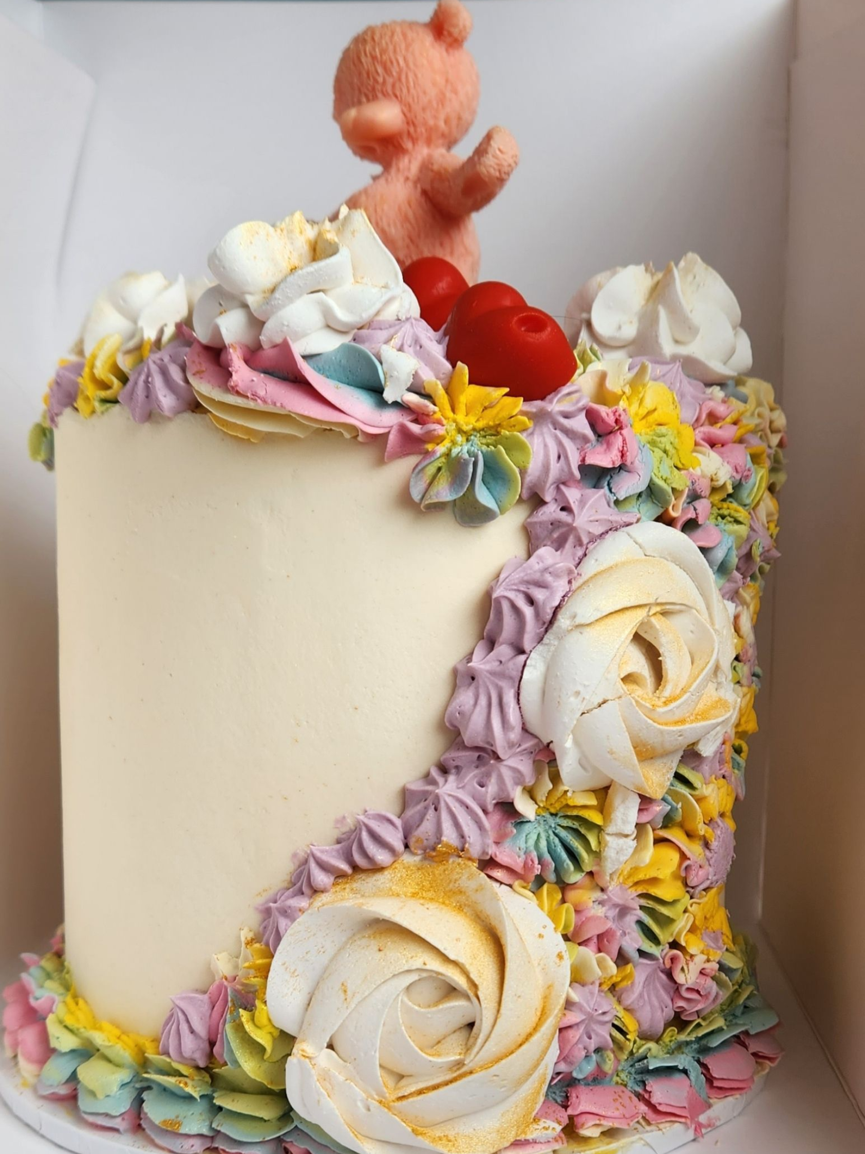 Cake with colorful buttercream flowers, bear figurine on top.